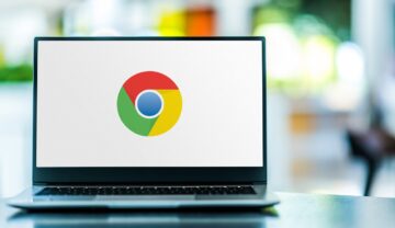 Logo-ul Google pe ecranul unui laptop, fundalul alb. Laptopul e gri, pe masă. Google a emis un avertisment recent pentru utilizatorii Chrome