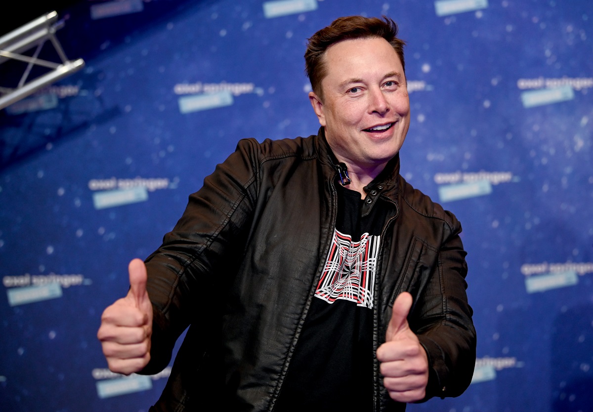Elon Musk pe covorul roșu al Premiilor Axel Springer, decembrie 2020. Poartă un tricou negru, cu o geacă neagră de piele, cu fundal albastru. Elon Musk și noua sa iubită au fost surprinși recent