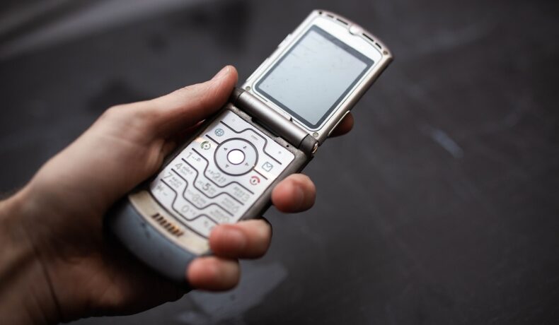 Motorola Rarz V3 pe argintiu, în mâna unui utilizator, cu fundal gri spre negru. Motorola Razr V3 e un telefon flip. E unul dintre cele mai vândute telefoane mobile din istorie