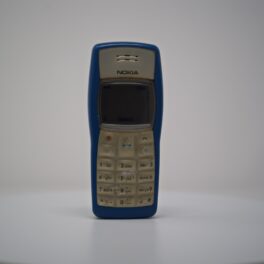 Telefonul mobil Nokia 1100 pe un piedestal alb, cu fundal alb. Modelul are carcasa albastră, tastele gri și ecranul închis