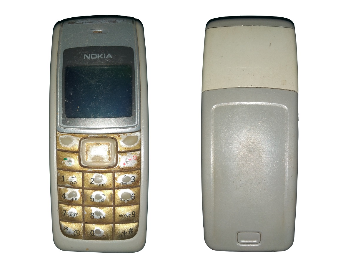 Telefonul mobil Nokia 1110 pe fundal alb. Modelul e gri, cu taste galbene, folosite, și ecranul închis