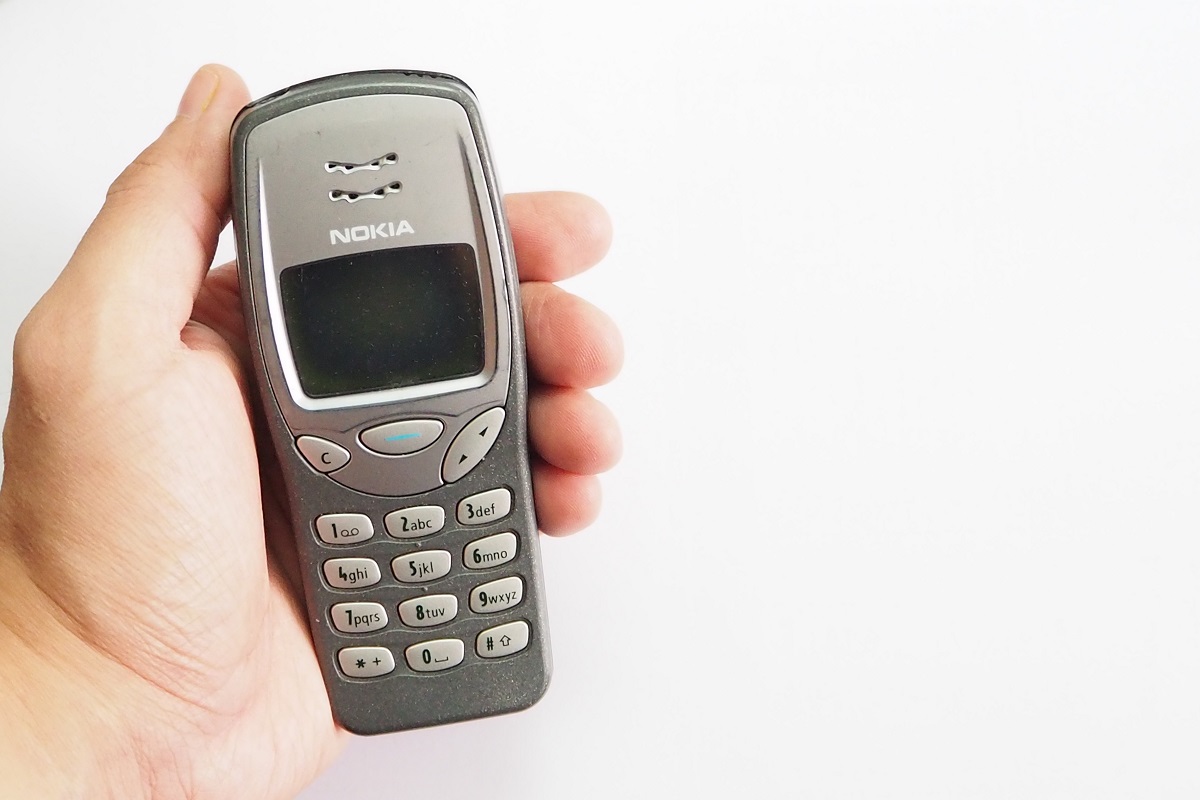 Telefonul mobil Nokia 3210 pe gri, ținut în mână, cu ecranul închis. Fundalul e alb