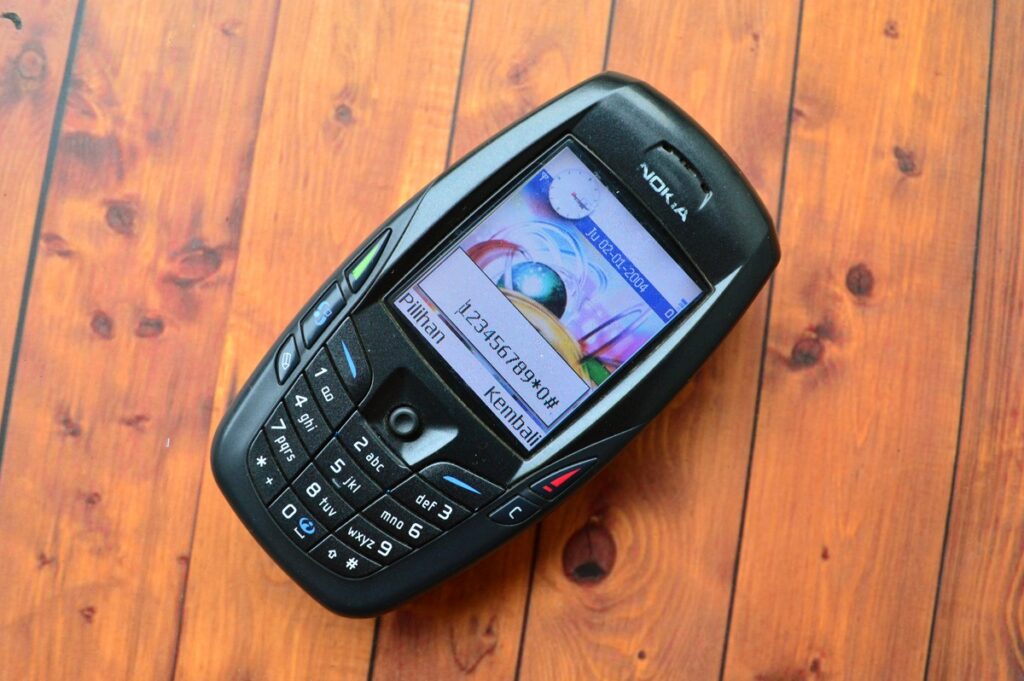Telefon mobil Nokia 6600 în culoare neagră, pe un fundal de lemn maro, cu ecranul deschis. Se numără printre cele mai vândute telefoane mobile din istorie