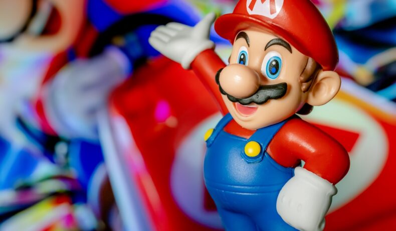 Personajul Mario, pe un fundal în ceață cu obiecte Mario. Figurina poartă salopetă albastră, bluză și șapcă roșii. Există multe detalii secrete din Super Mario Bros