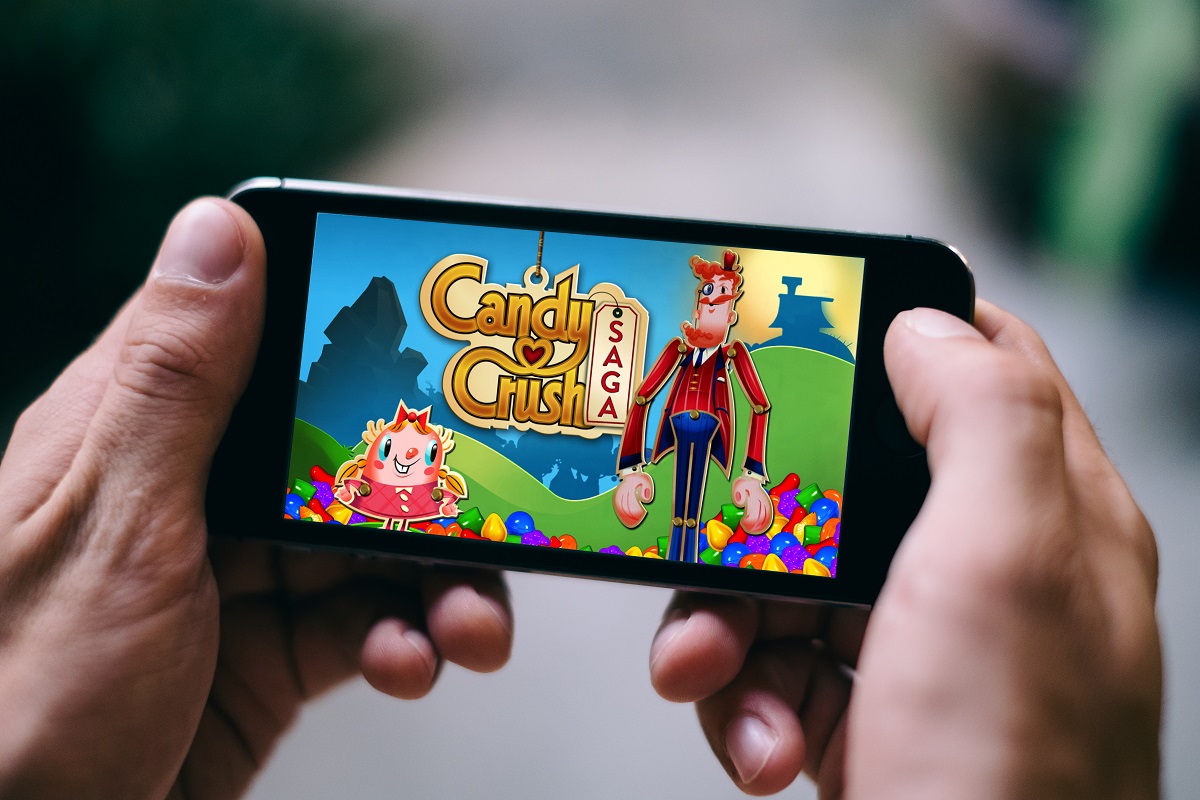Telefon mobil Android ținut în ambele mâini, cu jocul Candy Crush Saga pe ecran