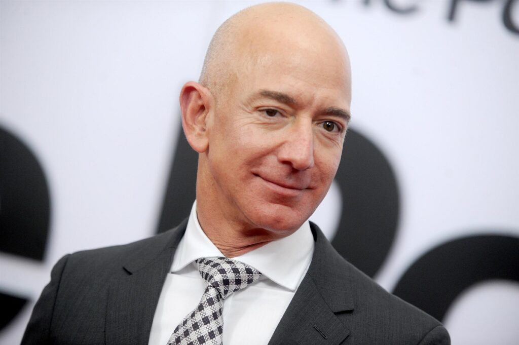 Jeff Bezos pe covorul roșu. E îmbrăcat într-un costum negru, cu o cămașă albă și cravată cu alb și negru. Fostul CEO Amazon a fost înlocuit de noul CEO Amazon, Andy Jassy