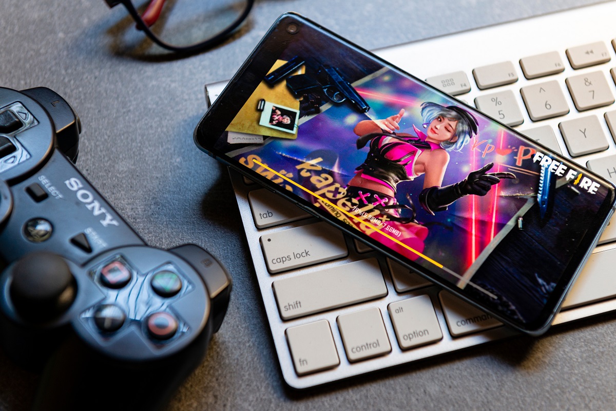 Garena Free Fire pe ecranul unui telefon Android, negru, care stă pe o tastatură albă. E un joystick negru lângă. Se numără printre cele mai descărcate jocuri Android