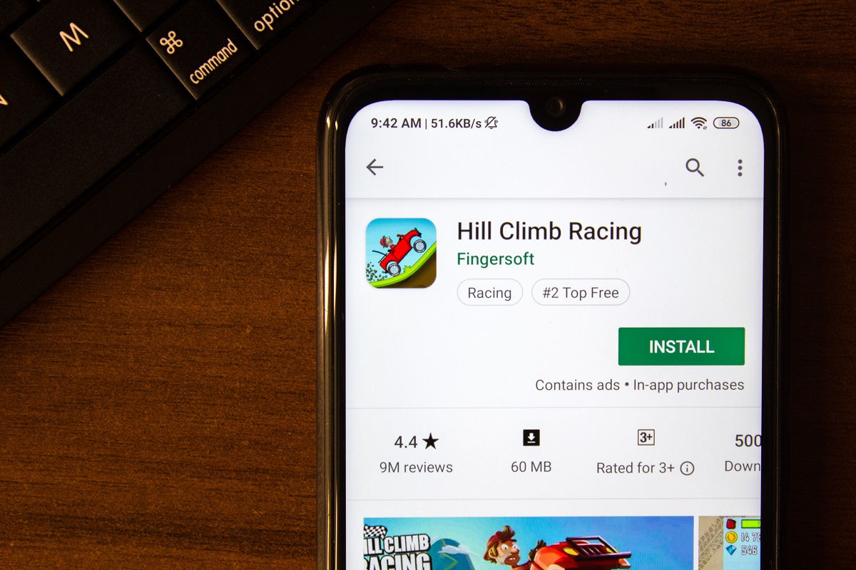Telefon mobil Android pe masă din lemn, cu jocul Hill Climb Racing pe ecran