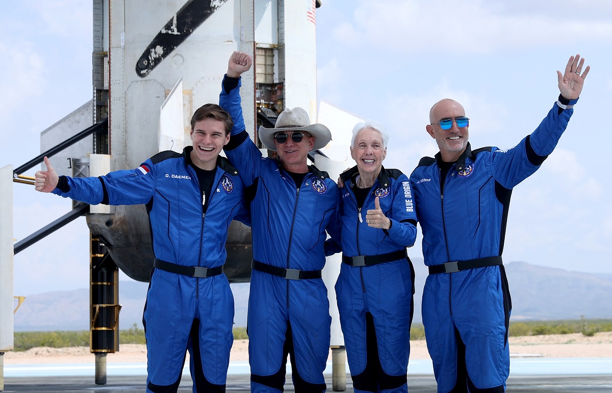 Jeff Bezos și echipa spațială Blue Origin, în anul 2021, toți poartă uniforme albastre. au o navetă spațială în spate