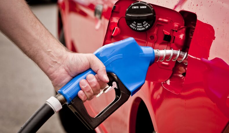 Bărbat care bagă benzină la pompă, într-o mașină roșie, cu o pompă albastră. Un studiu susține că bărbații contribuie mai mult la poluare
