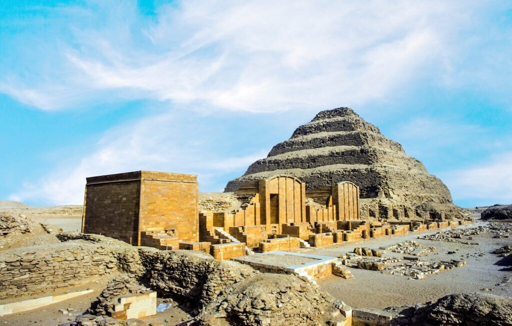 Piramida lui Djoser, una dintre cele mai vechi piramide din lume, fotografiată ziua. Tsructurile de la baza ei sunt galbene, piramida e bej, fundal cu cer albastru