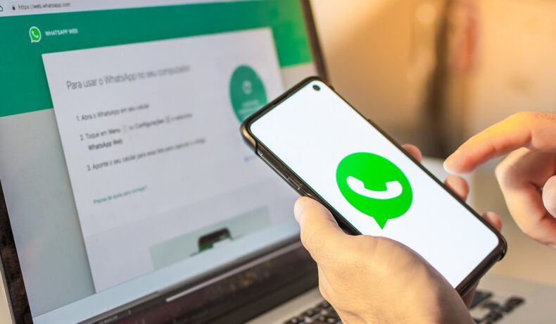 Imagine cu utilizator WhatsApp, care ține un smartphone în mână și are rețeaua de socializare deschisă pe laptop în față/ Platforma testează o opțiune prin care utilizatorii pot trimite mesaje WhatsApp fără telefon
