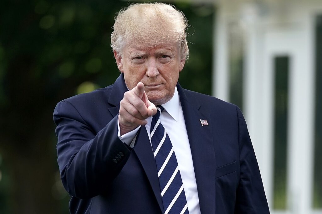 Donald Trump, fotografiat în fața Casei Albe, în iulie 2019. Poartă un costum albastru închis, cravată în dungi și arată cu degetul la cameră