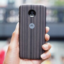Moto Z, fotografiat în 2016. Telefonul mobil are carcasă cu maro, negru și gri, spate, cu logo-ul Motorola, ținut în mână. Nu seamănă cu Moto G200 5G