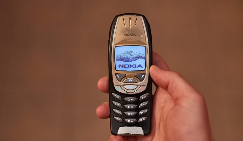 Telefon Nokia 6310 original, pe negru, ținut în mână, cu un fundal bej. Noua variantă Nokia 6310 a fost lansată în anul 2021