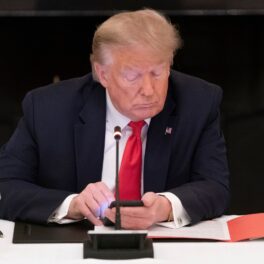 Donald Trump la o conferință de la Casa Albă. Stă la masă, pe scaun, are un smartphone în mână, se uită peste un dosar. Donald Trump va lansa o rețea de socializare în curând