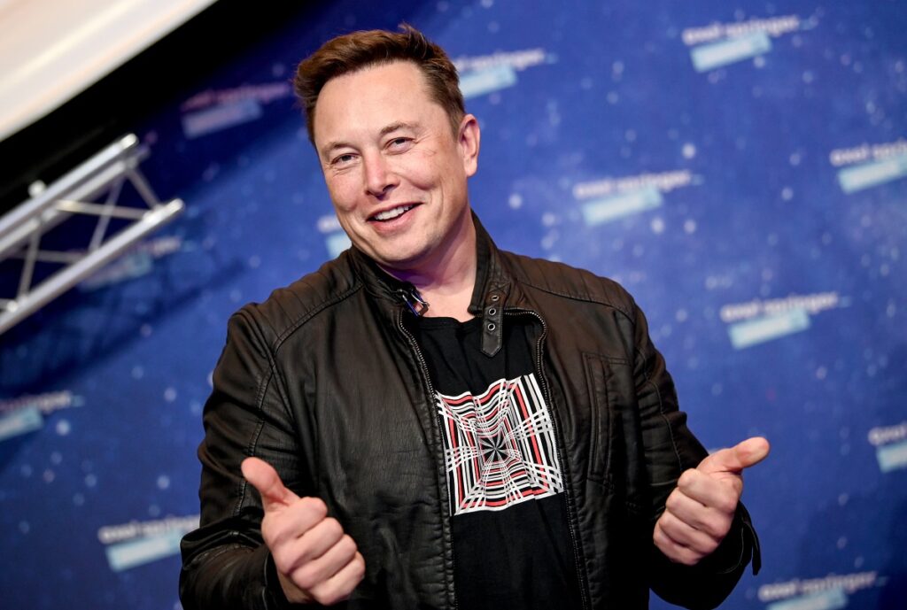 Elon Musk în anul 2020, oe covorul roșu al premiilor Axel Springer. E îmbrăcat într-o geacă neagră de piele, cu tricou negru, pe fundal albastru. Averea lui Elon Musk trece de 200 de miliarde de dolari