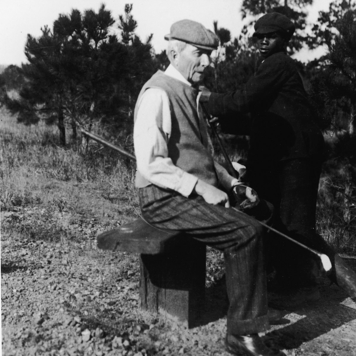 John D. Rockefeller, primul miliardar din SUA, la o rundă de golf. Stă pe o bîncuță și e ajutat de golf caddy de atunci, un băiat îmbrăcat în negru