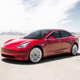 Mașină Tesla Model 3, culoare roșie, pe o pistă auto, cer însorit