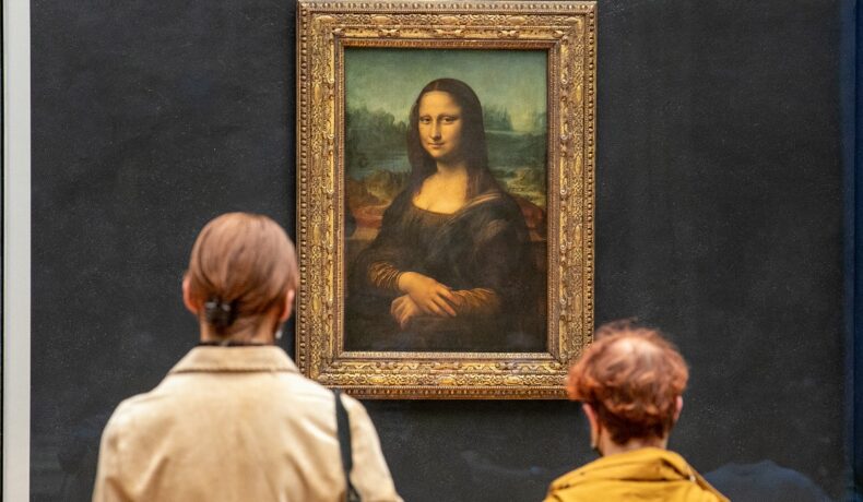 Mona LIsa (La Gioconda), creată de Leonardo da Vinci, expusă în muzeul Louvre. Peretele e albastru, rama e aurie, două persoane stau și se uită la ea
