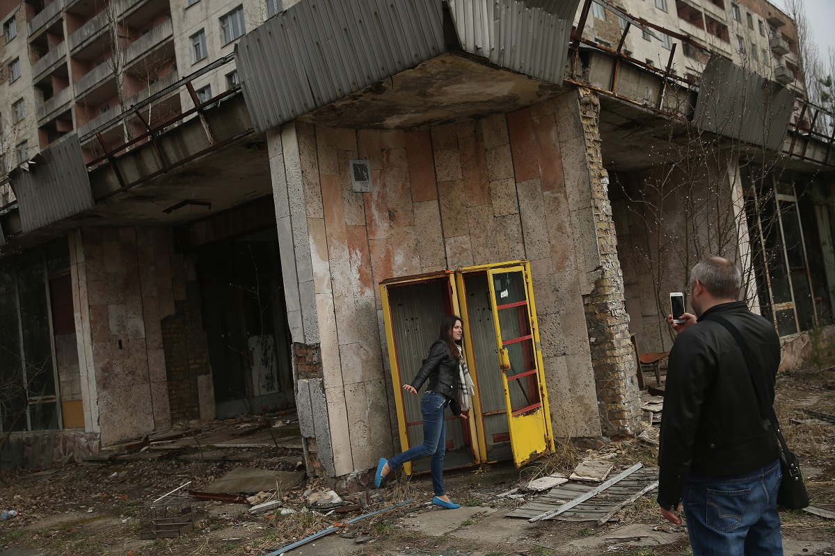 Turiști în Prîpeat, lângă Cernobîl, care se fotografiază lângă o clădire abandonată, o cutie telefonică galbenă