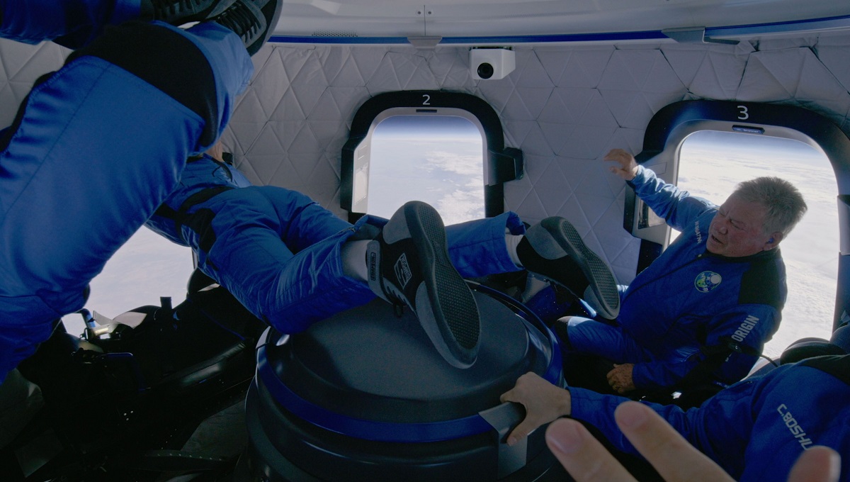 William Shatner alături de echipaj, la bordul navetei Blue Origin, octombrie 2021. Se află în zero gravitație și plutesc. Sunt îmbrăcați în albastru și plutesc
