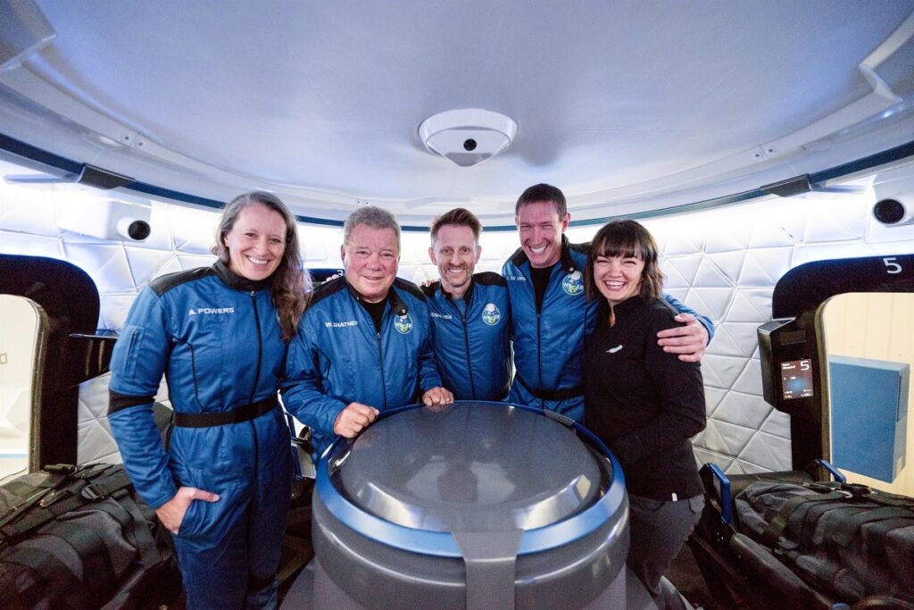 William Shatner fotografiat alături de Audrey Powers, Chris Boshuizen și Glen de Vries. Toți patru poartă uniforma albastră și se țin de mână. William Shatner a ajuns în spațiu la vârsta de 90 de ani