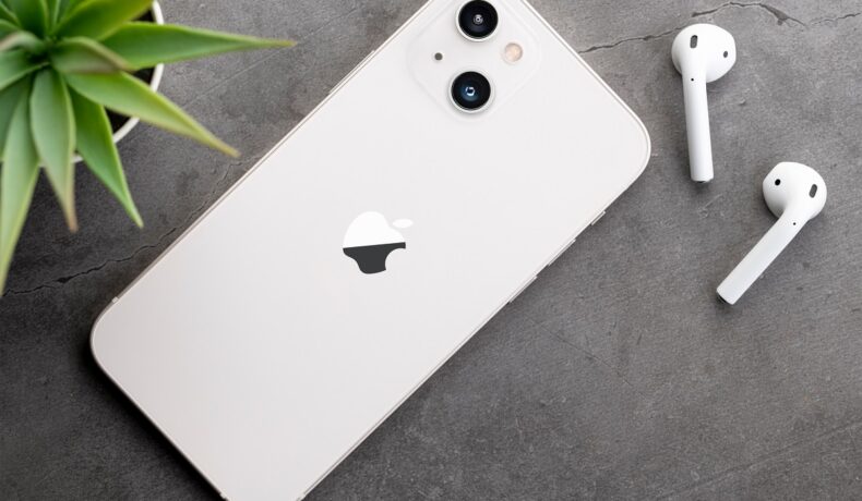IPhone 12 pe o suprafață gri. Carcasă e albă, are ângă niște căști albe și o plantă. Apple permite acum înlocuirea ecranului iPhone 13