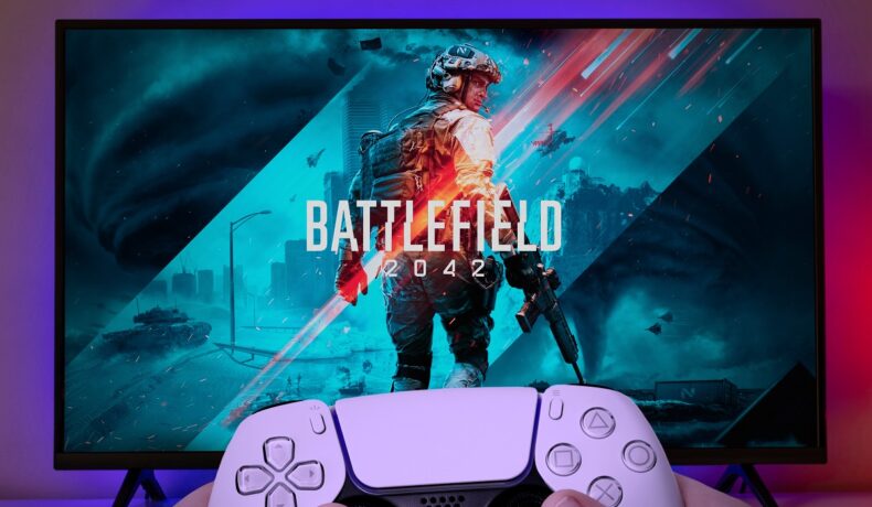 Imagine cu jocul Battlefield 2042 pe ecranul unui televizor, cu un controller de consolă de culoare albă în partea de jos a pozei. Battlefield 2042 e unul dintre jocurile cu cele mai multe recenzii negative