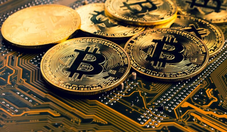 Monede Bitcoin aurii împrăștiate pe un procesor. Bitcoin a scăzut semnificativ după creșteri record
