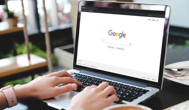 Persoană care căută pe motorul de căutare Google, pe un laptop negru cu gri, pe un birou. Unele căutări pe Google trebuie să fie evitate