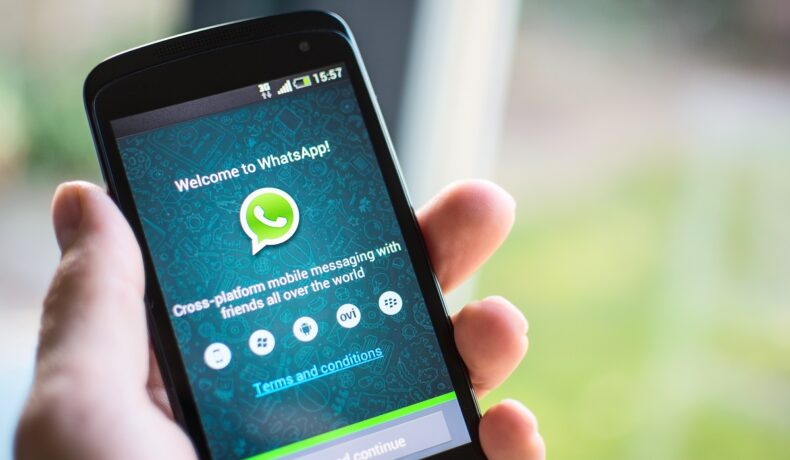 Aplicația WhatsApp pe ecranului unui telefon care e ținut în mână de un utilizator care știe ce e WhatsApp și cum se folosește