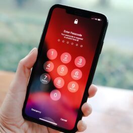 Telefon Iphone, cu ecran cu negru, roșu și portocaliu, ținut în mână. Codul secret iPhone e cunoscut la nivel internațional