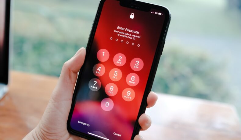 Telefon Iphone, cu ecran cu negru, roșu și portocaliu, ținut în mână. Codul secret iPhone e cunoscut la nivel internațional