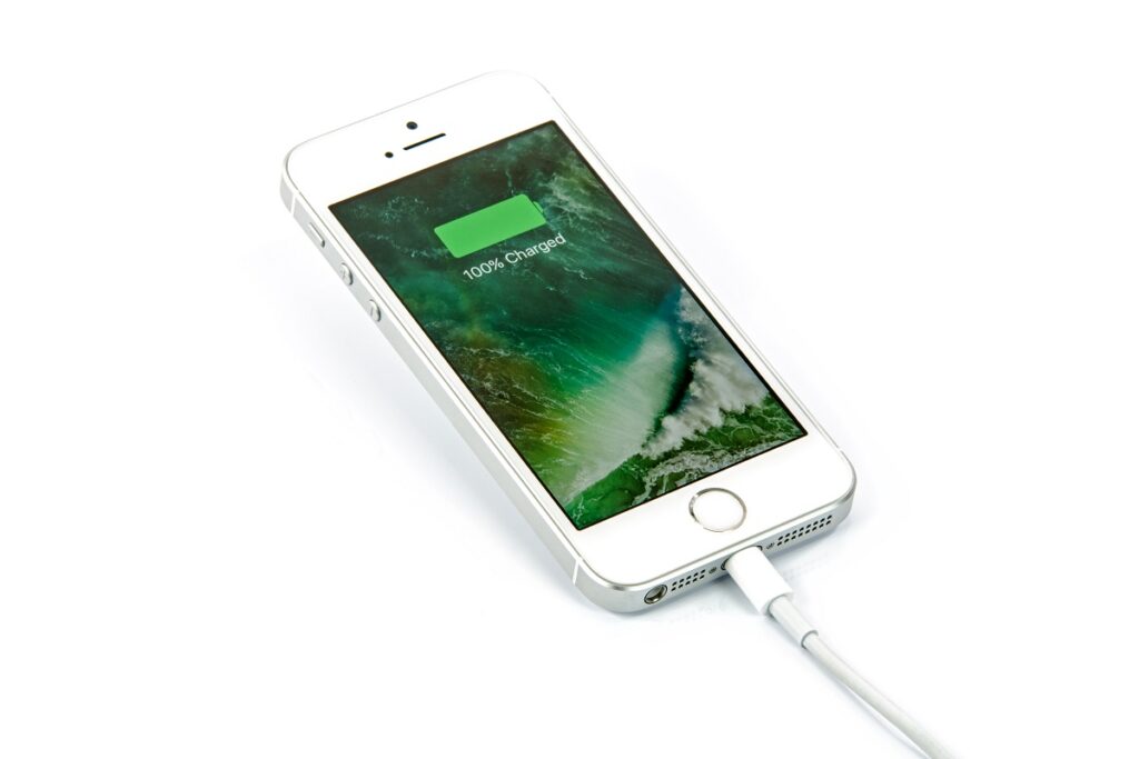 Telefon iPhone SE, în imagine oficială Apple, în care se află la încărcat. Telefonul e gri, ecranul e verde și arată procentul bateriei. Mulți se înreabă cum afli procentul bateriei la iPhone 13, dar există un truc simplu