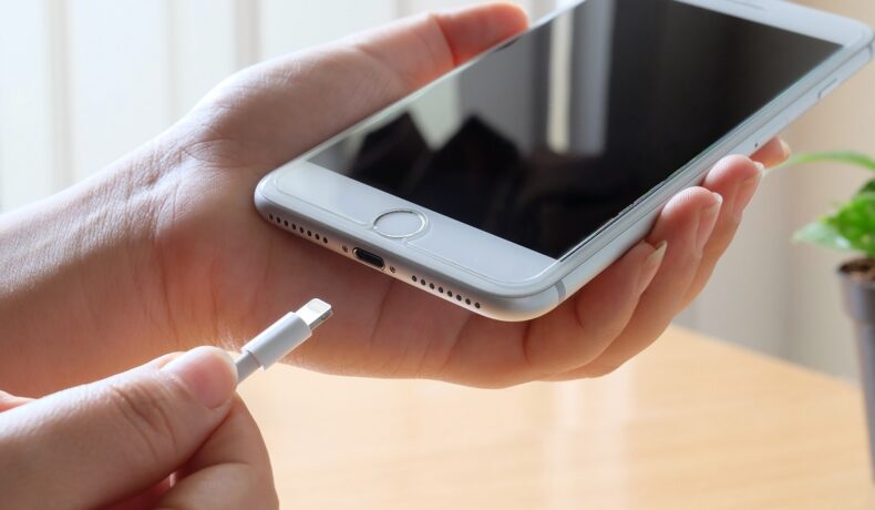 iPhone 7 în nuanță Space Gray, ținut în mână de un utilizator, care bagă telefonul la încărcat. Cum poți încărca iPhone-ul mai repede depinde de model