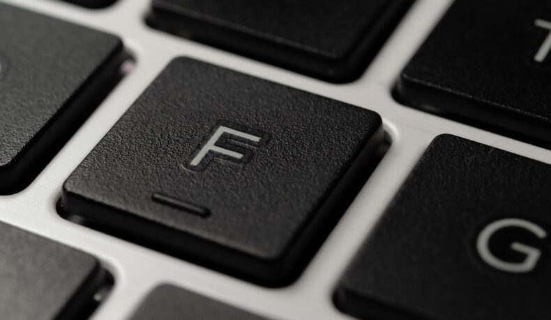 Close-up cu tastatura F, neagră, pe o tastatură cu fundal gri. Mulți se întreabă de ce au tastele f și j mici denivelări