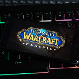 Emblema World of Warcraft Classic pe ecranul unui telefon cu o carcasă neagră, vcare stă pe o tastatură. Unele detalii World of Warcraft nu sunt cunoscute de multi jucatori