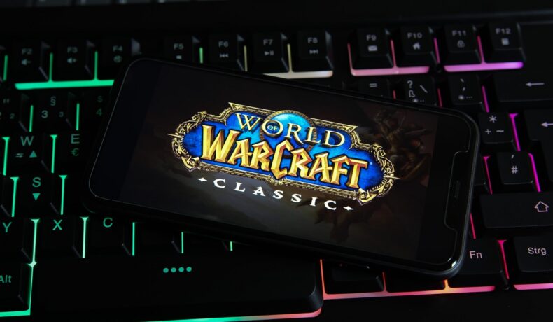 Emblema World of Warcraft Classic pe ecranul unui telefon cu o carcasă neagră, vcare stă pe o tastatură. Unele detalii World of Warcraft nu sunt cunoscute de multi jucatori