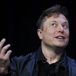 Elon Musk, la o conferință SpaceX din 2020. Poartă un costum negru, cu o cămașă neagră, pe fundal e negru. Elon Musk a vândut milioane de acțiuni Tesla