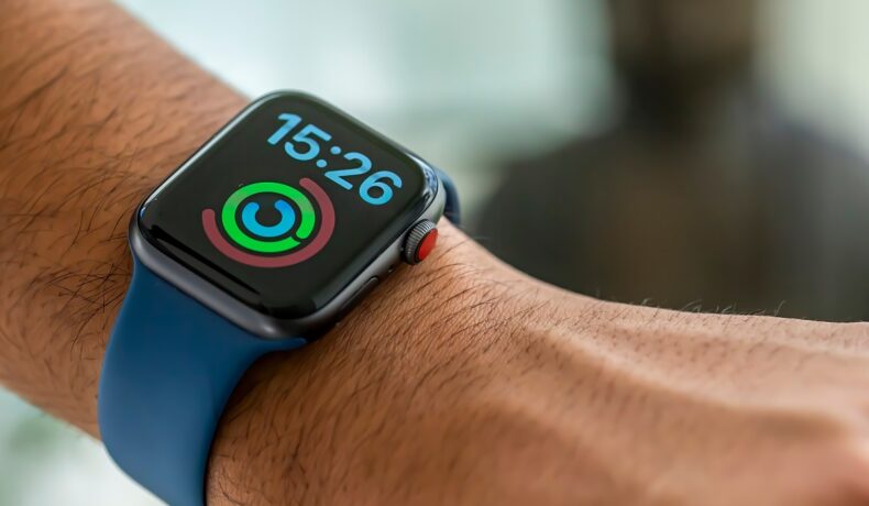 Ceas smart Apple Watch Series 4, cu sistem de operare WatchOS 7. Ceasul are curea albastră, ecran negru, e pe mână. Se numără printre unele gadget-uri ideale pentru cadouri de sărbători