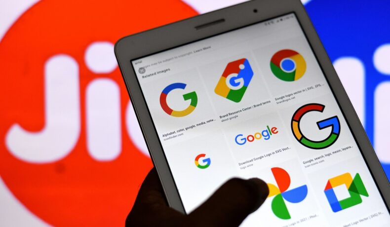 O tabletă pe care se află aplicațiile google în timp ce este ținută în mână în fața unui logo al companiei Jio