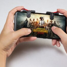 Telefon ținut cu ambele mâini de un jucător. Pe ecran apare logo-ul jocului PlayerUnknown's Battlegrounds, unul dintre acele jocuri iPhone gratuite
