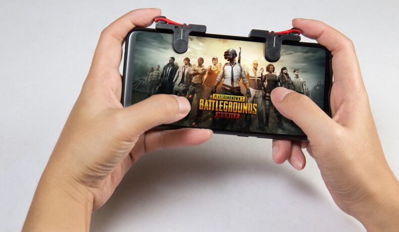Telefon ținut cu ambele mâini de un jucător. Pe ecran apare logo-ul jocului PlayerUnknown's Battlegrounds, unul dintre acele jocuri iPhone gratuite