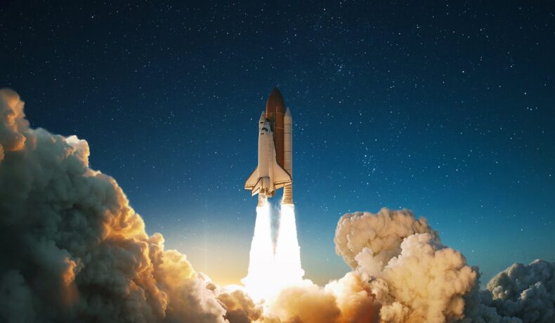 Navă spațială care e lansată în spațiu. Racheta e roșie, nava e albă, sunt nori în partea de jos a imaginii. În noiembrie 2021, NASA lansează o misiune istorică, numită DART