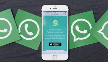 Telefonul cu o carcasă albă care are WhatsApp pe ecran, pe o masă gri închis, cu patru simboluri WhatsApp lângă el. Opțiuni secrete WhatsApp nu sunt cunoscute de toți utilizatorii