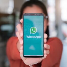 Telefon ținut în mână cu WhatsApp pe ecran, ținut de o femeie îmbrăcată în portocaliu. WhatsApp introduce noi opțiuni pentru protejarea datelor personale
