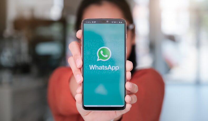 Telefon ținut în mână cu WhatsApp pe ecran, ținut de o femeie îmbrăcată în portocaliu. WhatsApp introduce noi opțiuni pentru protejarea datelor personale