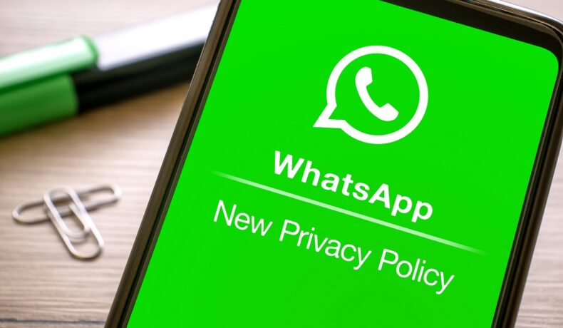 WhatsApp pe ecranul unui telefon, cu schimbarea privacy policy (politica de confidențialitate) Ecranul e verde, carcasa telefonului e neagră, pe fundal apare un birou. WhatsApp schimbă iar politica de confidențialitate în Europa