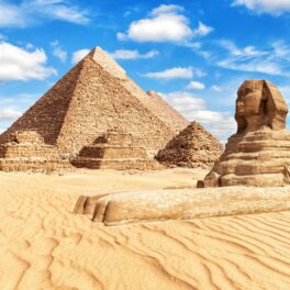 Piramidele din Giza și celebrul Sfinx, construite în deșert, cu cerul albastru pe fundal
